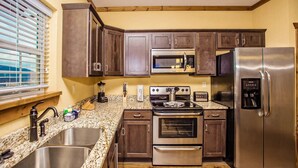 A kitchen with dark wooden cabinets, stainless steel appliances, granite countertops, and a window with blinds.