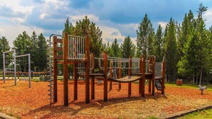 A playground with swings, a slide, and climbing structures surrounded by trees.