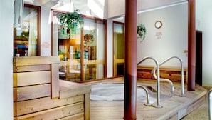 Una terraza de madera con un jacuzzi, barandillas metálicas y puertas de vidrio con plantas.