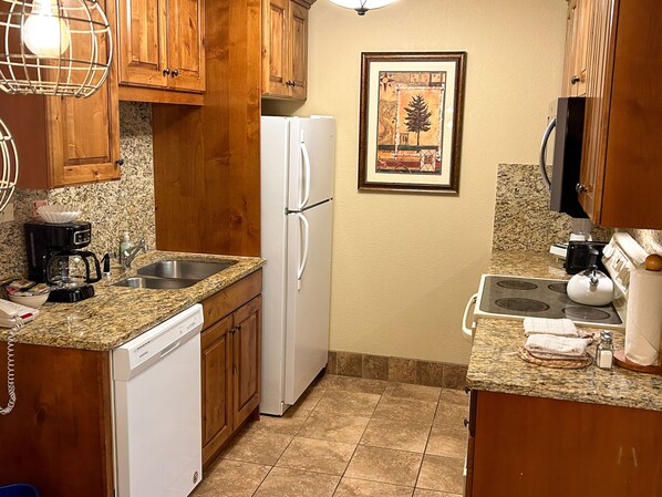 A compact kitchen with wooden cabinets, a white refrigerator, a coffee maker, and a microwave.