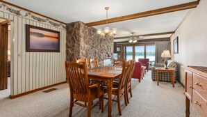 A dining area with a wooden table and chairs, a chandelier, and a view through the window. - Point Condos 2BR w/ Lake Views & Fireplace (Breezy Point)