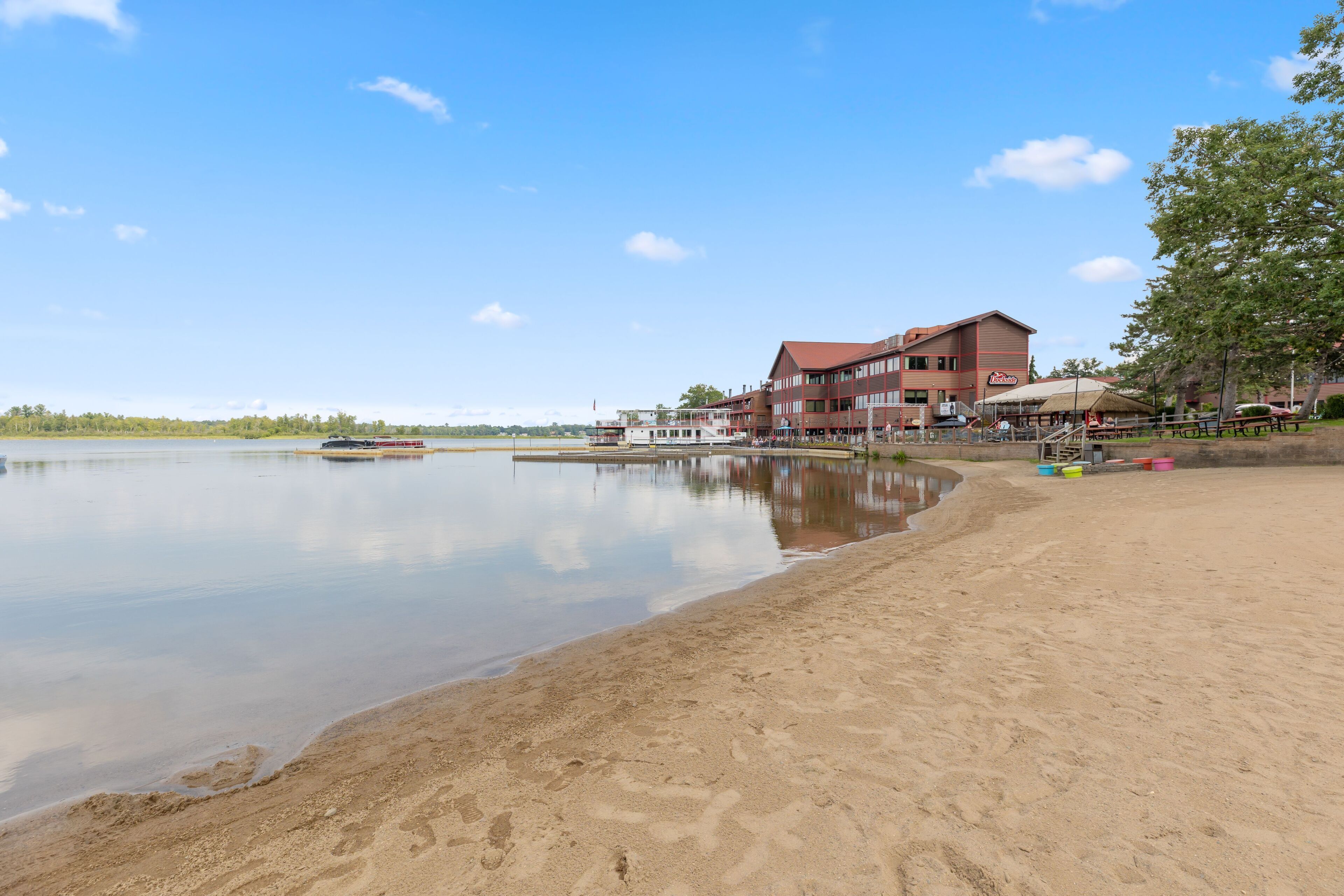 Un hôtel situé au bord d’un lac, doté d’une plage de sable, d’un quai pour bateaux et d’un grand bâtiment avec de nombreuses fenêtres et un toit rouge.