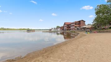 Un hôtel situé au bord d’un lac, doté d’une plage de sable, d’un quai pour bateaux et d’un grand bâtiment avec de nombreuses fenêtres et un toit rouge.