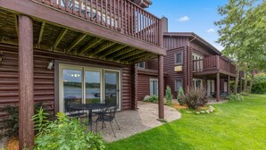 A log cabin with a balcony, a patio with a table and chairs, and a well-maintained lawn. - Point Condos 2BR w/ Lake Views & Fireplace (Breezy Point)