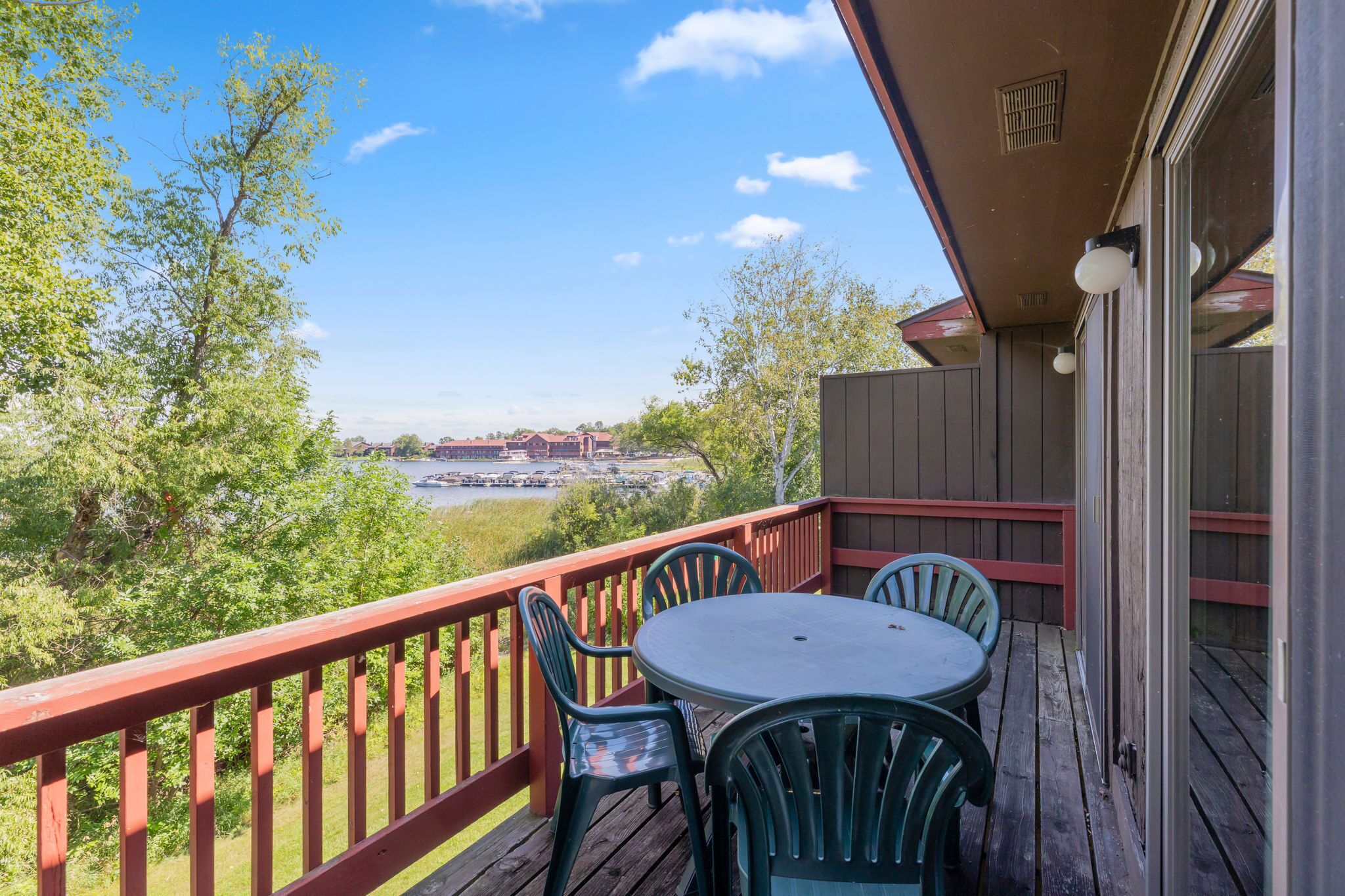 A wooden deck with a table and chairs, overlooking a river and distant buildings.