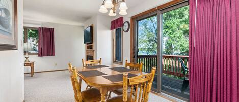 A dining area with a wooden table and chairs, a chandelier, a clock, and a large window with curtains.