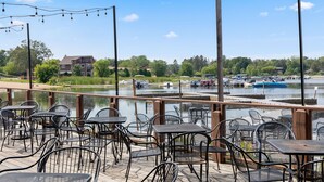 An outdoor seating area with tables and chairs overlooking a body of water with boats.