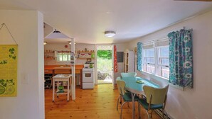Una cocina compacta con comedor, piso de madera y vista a un jardín por una puerta abierta.