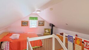 Un dormitorio acogedor en el ático, con techo inclinado, una cama individual, una silla, una mesita y un calendario en la pared.