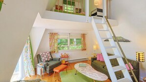 Un habitación estilo loft con escalera, sofá, mesa de centro y ventana con cortinas.