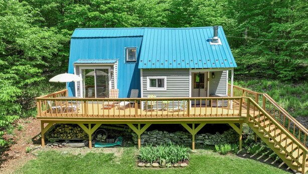 Una casa de dos pisos con techo azul y terraza de madera.