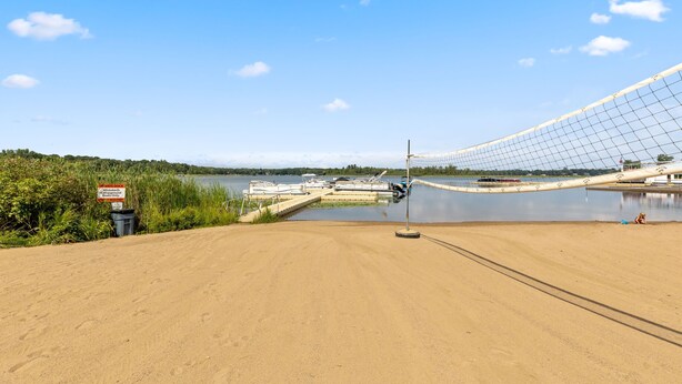 A sandy beach area with a netted structure, a sign indicating a mooring dock, and boats in the background.