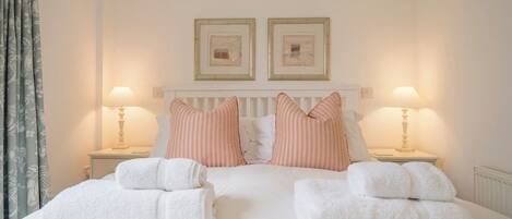 A double bed with white linens, two striped pillows, and two white towels. There are two bedside tables with lamps and framed pictures above the bed.