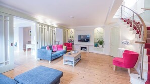 Ein modernes Wohnzimmer mit einem blauen Sofa, roten Sesseln, einem Holztisch und einem an der Wand befestigten Fernseher.