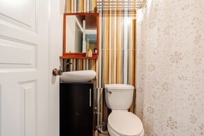 A bathroom with a striped wall, a toilet, a sink, and a mirror.
