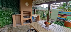 An outdoor patio with a wooden table, chairs, a small grill, and a decorative wall.