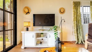 Un soggiorno con una TV su un mobile bianco, una pianta, una lanterna e una finestra con tende.
