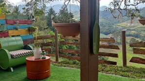 Zona relax all'aperto con un divano verde, un fusto rosso e una recinzione in legno con vista su una valle rigogliosa.