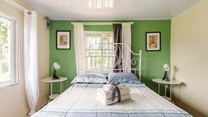 Un letto rifatto con coperta a righe, due comodini con lampade, una finestra con tende e due quadri appesi alle pareti.