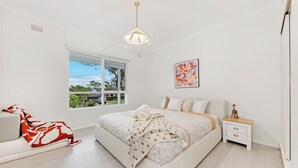 A bedroom with a bed, bedside table, nightstand, window, and a view of the outdoors.