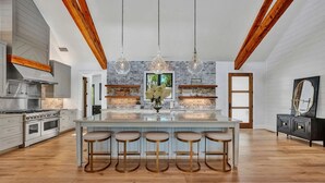 A modern kitchen with a central island, bar stools, hanging crystal chandeliers, and a brick accent wall. - Private Dock, 30 day rentals (Union Hall)