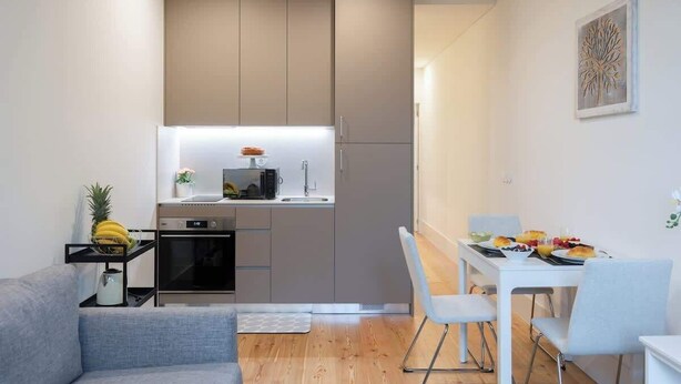 A compact kitchen with modern appliances, a dining area with a table and chairs, and a small seating area with a sofa. - Cozy & Bright Flat by Host Wise (Guimarães)
