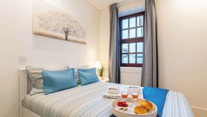 A hotel room with a bed, a tray with breakfast items, a window with curtains, and a wall-mounted artwork. - Cozy & Bright Flat by Host Wise (Guimarães)