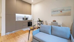 A modern living room with a sofa, a dining table with chairs, a kitchen area with cabinets, and a painting on the wall. - Modern & Cozy Flat by HostWise (Guimarães)