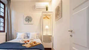 A neatly arranged bedroom with a bed, a bedside table with a lamp, a hanging wardrobe, and a tray with drinks and snacks on the bed. - Modern & Cozy Flat by HostWise (Guimarães)