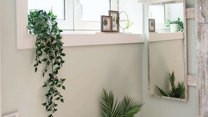 A bathroom with a window, a mirror, and a plant on a wooden dresser.