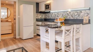 A modern kitchen with a white refrigerator, a microwave, a marble backsplash, and a small bar area with white chairs.