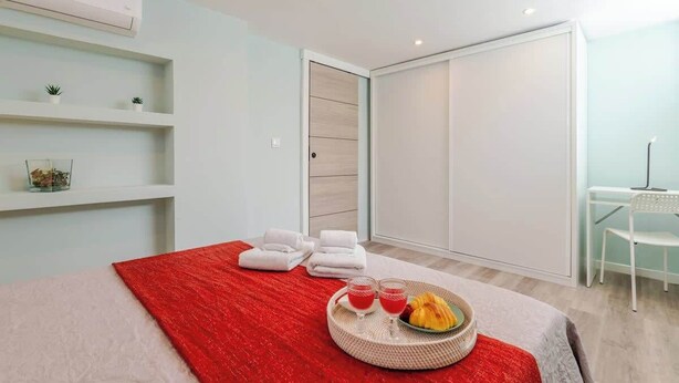 A modern hotel room with a bed, a red throw, towels, a breakfast tray, and a desk with a chair.