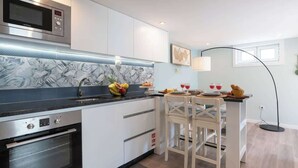 A modern kitchen with white cabinets, a black countertop, and a microwave. There is a dining area with a table and chairs, and a floor lamp.