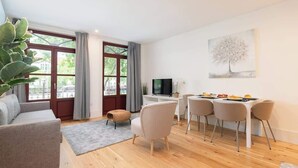 A modern living room with a sofa, dining table, chairs, a TV, and a large window with curtains.