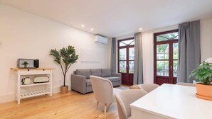 A modern living room with a grey sofa, a white dining table, and a wooden floor.