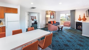 A modern hotel room with a dining area, a living room with a sofa and armchairs, a kitchen with wooden cabinets, and a fireplace. - Palm Springs Condos (Palm Springs)