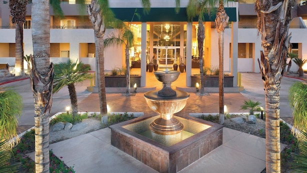 A hotel entrance with a central fountain, palm trees, and a well-lit building facade. - Palm Springs Condos (Palm Springs)