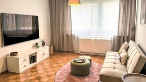 Una sala de estar con televisión de pantalla plana, un sofá, una mesa de centro y una ventana con cortinas.