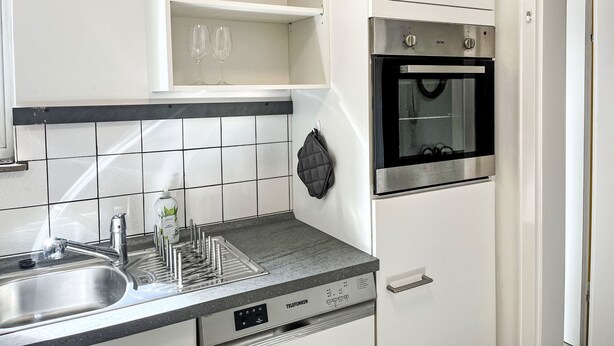 Una cocina con un lavamanos de acero inoxidable, horno empotrado y salpicadero de azulejos.