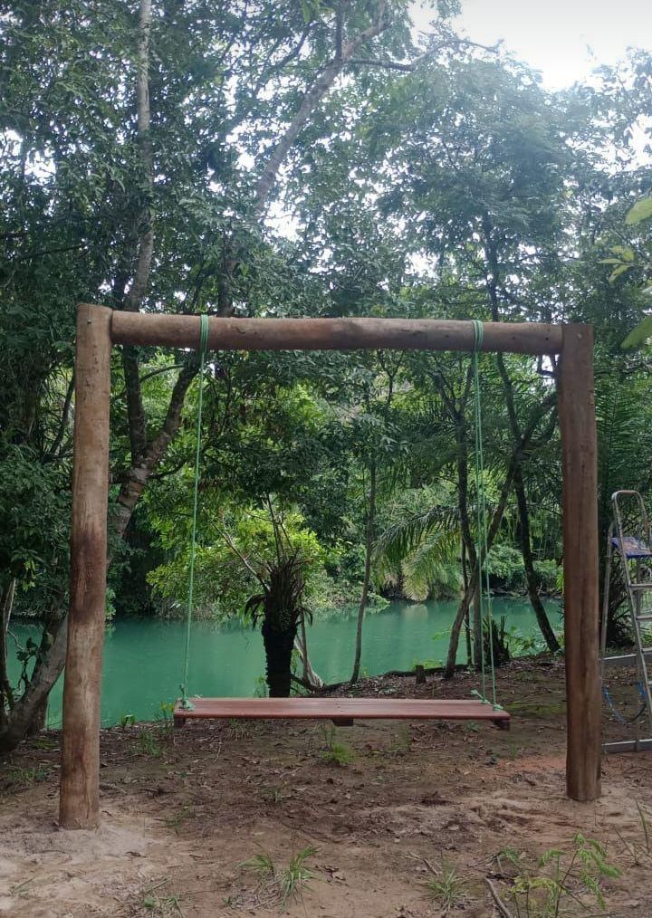 Um conjunto de baloiço de madeira num ambiente natural, com uma extensão de água verde ao fundo.