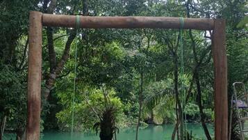 Um conjunto de baloiço de madeira num ambiente natural, com uma extensão de água verde ao fundo.