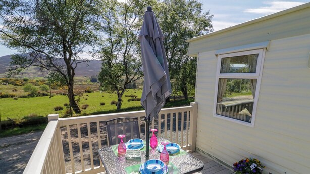 Een overdekt terras met een tafel voor vier personen, een fiets en een uitzicht op een groen landschap.