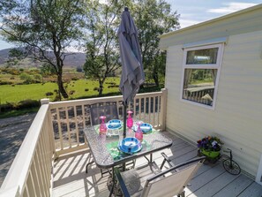 A covered outdoor patio with a table set for four, a bicycle, and a view of a green landscape. - The Caravan@meenacross (Larganreagh Barr)