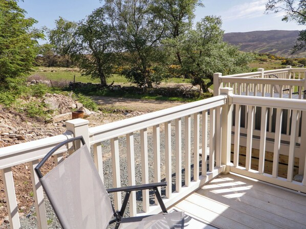 A wooden deck with white railings overlooking a natural landscape with trees and a stone wall. - The Caravan@meenacross (Larganreagh Barr)