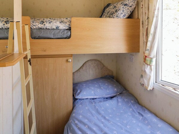 A bunk bed with a wooden ladder, a lower single bed with a blue patterned sheet, and a window with curtains. - The Caravan@meenacross (Larganreagh Barr)