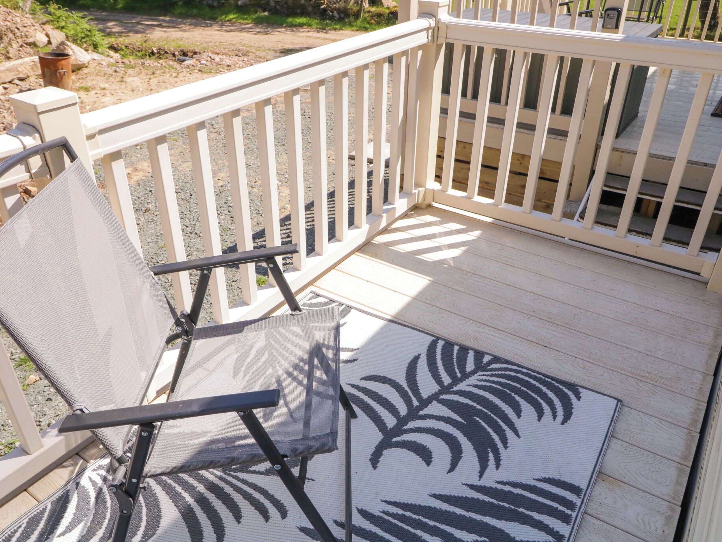Eine Holzterrasse mit weißer Brüstung, ein Sessel mit blattmusterbezogenem Kissen und ein kleiner Blumentopf.