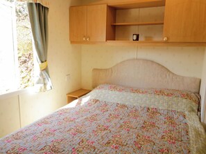 Une chambre à coucher avec un lit, une tête de lit en bois, une fenêtre avec des rideaux et une étagère au-dessus du lit.