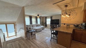 A spacious living area with a large sofa, a dining table, and a kitchen area with a countertop and appliances. - Cozy Farmhouse Getaway 10 min from Lost Island and Casino (La Porte City)