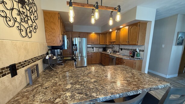 A modern kitchen with granite countertops, stainless steel appliances, wooden cabinets, and pendant lighting. - Cozy Farmhouse Getaway 10 min from Lost Island and Casino (La Porte City)