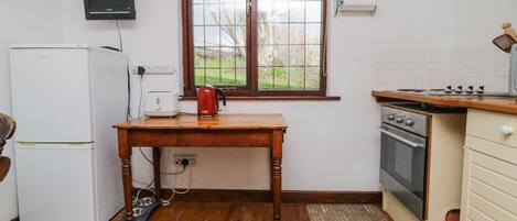 Eine kleine Küche mit einem Kühlschrank, einem Toaster, einem Wasserkocher, einem Fenster mit Blick auf Bäume, einem Herd und einem Spülbecken.